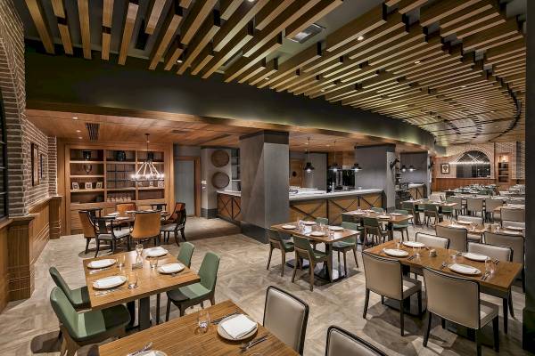 Innenansicht des Restaurants im Titanic Luxury Collection Bodrum Hotel mit Holztischen, Stühlen und einem offenen Bereich mit einer Bar.