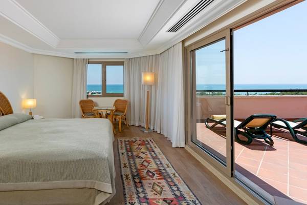 Xanadu Resort Hotel Zimmer mit Meerblick, Bett, Tisch, Stühle, Lampen und Terrasse mit Sonnenliegen.