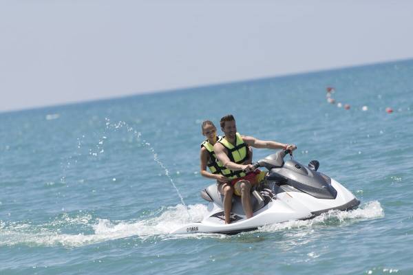 Zwei Leute fahren ein Jetski im Meer, beide tragen gelbe Sicherheitswesten.