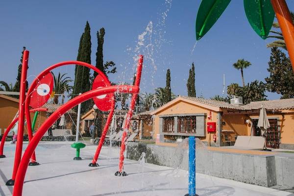 Außenbereich des Pools im Suites & Villas By Dunas Hotel mit bunten Wassersprudlern und Gebäuden im Hintergrund.