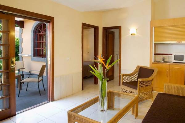Innenansicht des Suites & Villas By Dunas Hotel mit Wohnzimmer, Couch, Tisch, Stühlen und Küche.