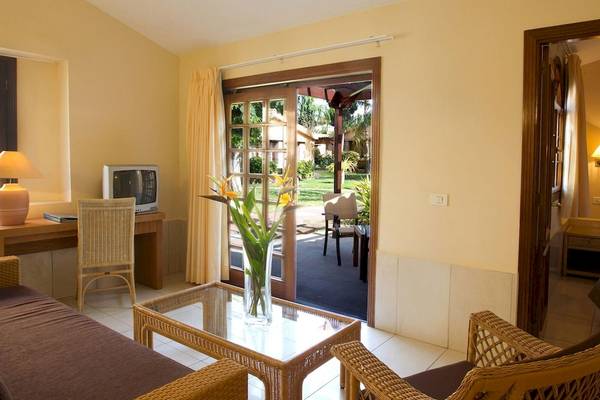 Innenansicht eines Zimmers der Suites & Villas By Dunas mit Wohnzimmer, Esstisch, Fernseher und Balkon.