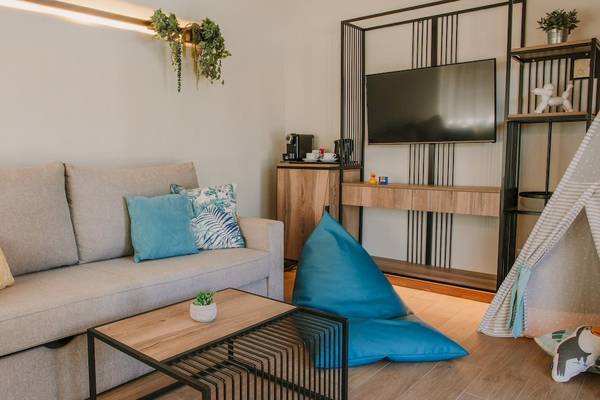 Wohnzimmer mit Sofa, Kissen, Couchtisch, Fernseher und Regal in einem Hotelzimmer.