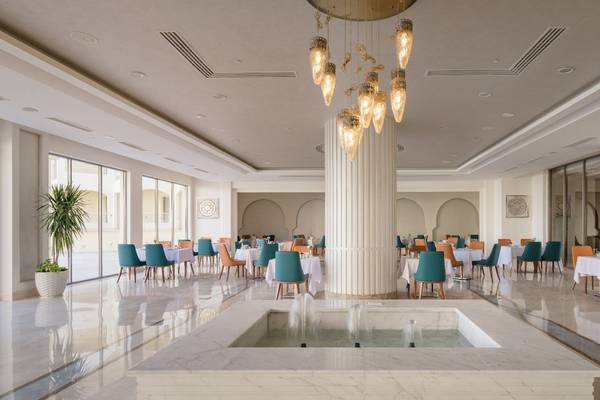 Innenbereich des Xanadu Makadi Bay Hotels mit modernem Restaurant, Wasserbrunnen und vielen Tischen und Stühlen.