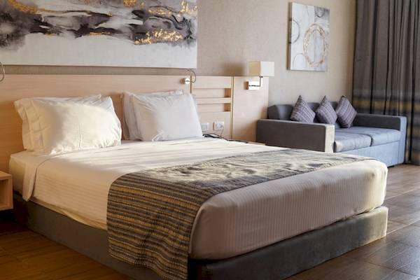 Hotelzimmer im Xanadu Makadi Bay mit zwei Betten, Kissen, einem Tisch, einer Couch und Kunstwerken an der Wand.