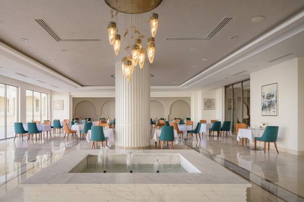 Innenbereich des Xanadu Makadi Bay Hotels mit modernem Design, großen Tischen und Stühlen, einer zentralen Säule und einem Wasserbrunnen.