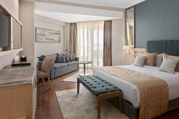 Innenansicht eines Hotelzimmers im Xanadu Makadi Bay mit einem großen Bett, einem Sofa, einem Fernseher und einem Schreibtisch.