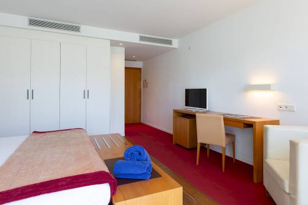 Innenansicht eines Hotelzimmers im Aimia Hotel mit Bett, Schreibtisch und roten Teppich