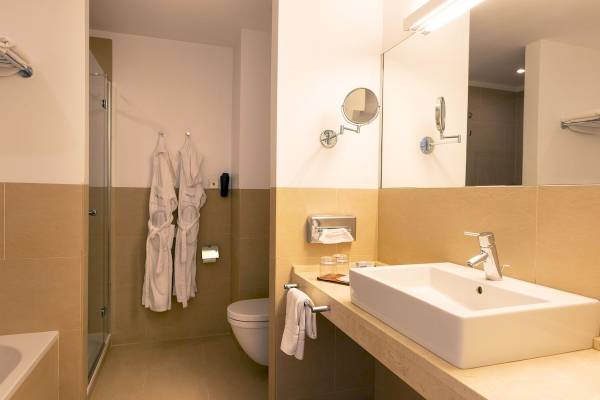 Badezimmer im Aimia Hotel mit Badewanne, Toilette, Waschbecken und Spiegeln.