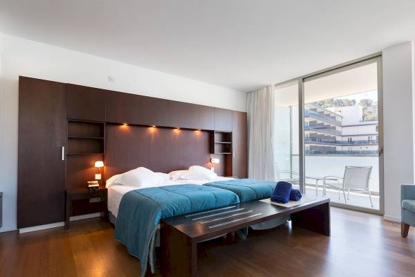 Schlafzimmer im Aimia Hotel mit zwei Betten, dunklem Holzboden und großen Fenstern.
