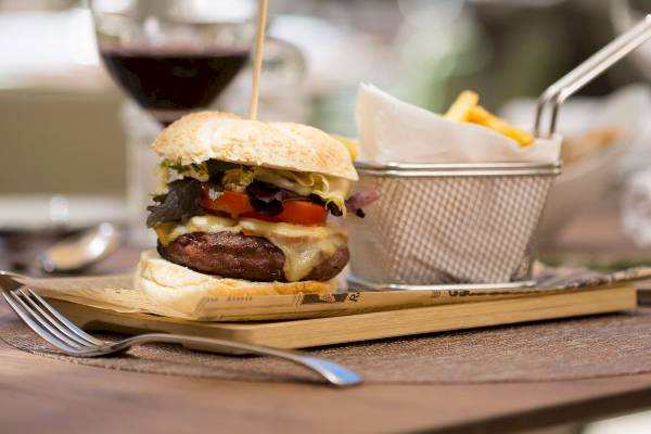 Ein Burger mit Pommes auf einer Holzplatte im Aimia Hotel.