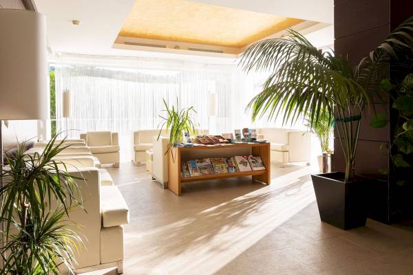 Empfangsbereich des Aimia Hotels mit weißen Sofas, Büchern auf dem Tisch und großen Pflanzen.