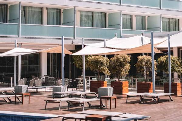 Außenbereich des Aimia Hotels mit Loungemöbeln, Sonnenschirmen und Bäumen.
