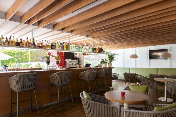 Innenansicht der Bar des Aimia Hotels mit Holzmöbeln, einer Theke und Pflanzen.