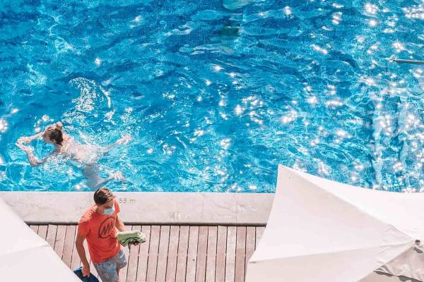 Aussicht auf das Schwimmbad des Aimia Hotels mit Gästen, die schwimmen und einer Person, die Handtücher hält.