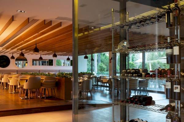 Innenansicht des Restaurants im Aimia Hotel mit Tischen, Stühlen und Pflanzen in der Mitte.