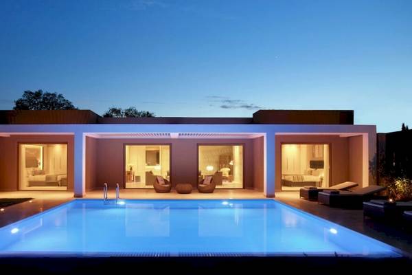 Nachtansicht der Ikos Dassia Villa mit beleuchtetem Pool und offenen Fenstern.