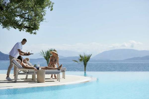 Gäste entspannen in Liegestühlen am Pool, ein Mitarbeiter serviert Getränke.