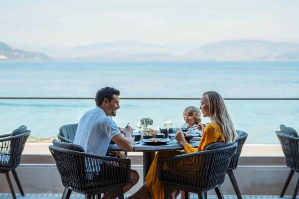 Eine Familie sitzt am Tisch mit Meerblick im Ikos Dassia und genießt ihr Essen.
