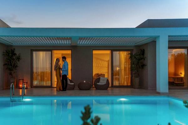 Ein Paar steht abends vor dem Ikos Dassia Hotel und blickt auf den Swimmingpool.