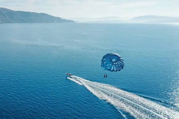 Zwei Personen parasailing über dem Meer vor dem Ikos Dassia Hotel.
