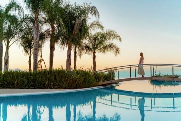 Eine Frau steht auf einer Brücke über einem Pool im Hotel Ikos Dassia.