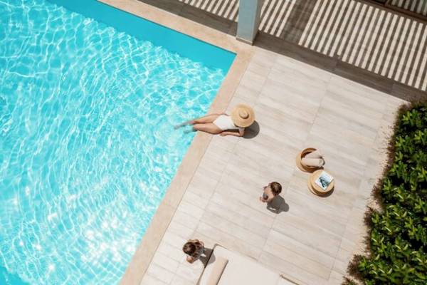 Luftaufnahme eines Pools mit Gästen im Hotel Ikos Dassia, einer Frau schwimmt und zwei Kinder sitzen neben dem Pool.