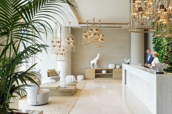 Empfangsbereich des Ikos Dassia Hotels mit modernem Design, weißen Möbeln, Pflanzen und einer Statue.