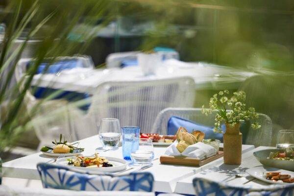 Außenterrasse des Ikos Odisia Hotels mit gedeckten Tischen und Stühlen, Tellern mit Essen und Getränken.