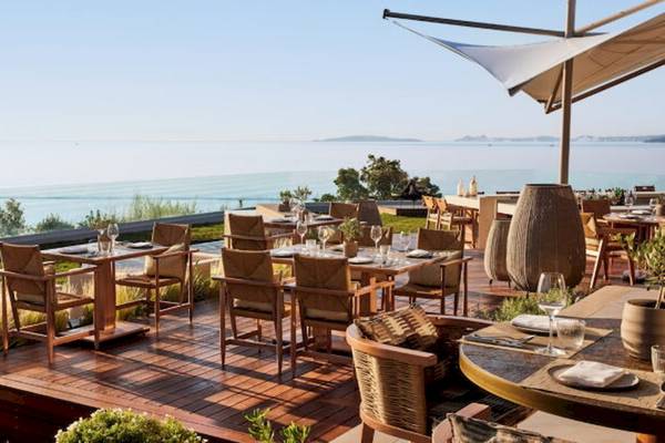 Außenterrasse des Ikos Odisia Hotels mit Blick auf das Meer und Tischen im Freien