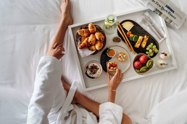 Eine Person genießt Frühstück auf einem Bett mit Croissants, Obst und anderen Leckereien.