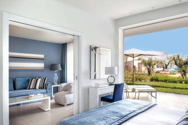 Innenansicht eines Zimmers im Ikos Olivia Hotel mit blauer Couch, Schreibtisch und großer Terrasse.
