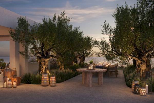 Terrasse des Ikos Olivia Hotels mit Olivenbäumen und Tisch, umgeben von Laternen.