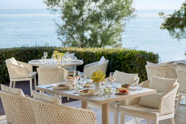 Terrasse des Ikos Olivia Hotels mit Blick auf das Meer und weißen Stühlen und Tischen.
