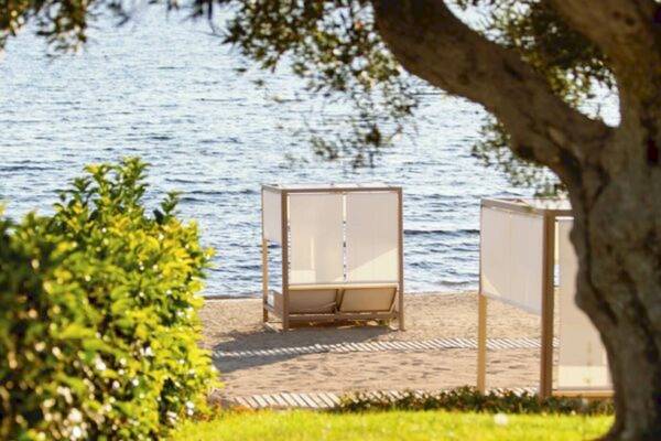 Zwei Loungebetten am Strand neben einer Bucht mit Wasser und Pflanzen.