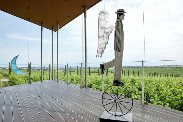 Statue eines Mannes auf Einrad auf Terrasse vor Weinberg bei Ikos Olivia Hotel