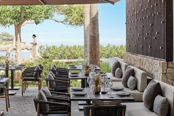 Terrasse im Ikos Porto Petro Hotel mit Blick auf das Meer und eine Frau im Hintergrund.