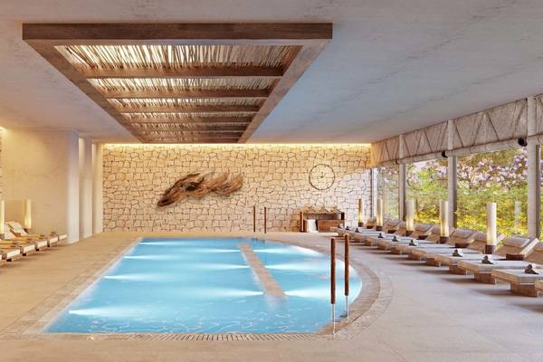 Innenpool des Ikos Porto Petro Hotels mit Steinwänden und Holzmöbeln.