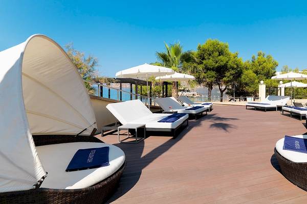 Loungebereich des H10 Blue Mar Boutique Hotels mit weißen Liegen und Sonnenschirmen.