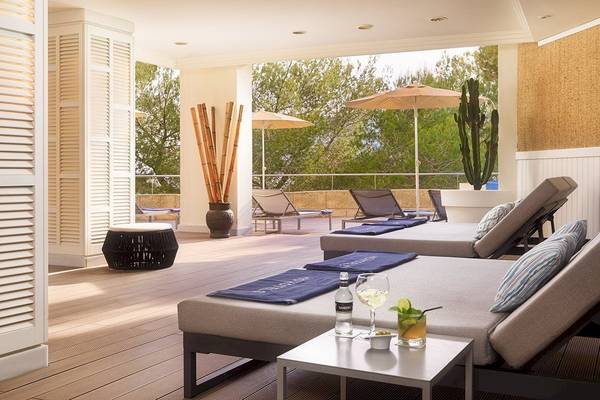 Terrasse des H10 Blue Mar Boutique Hotels mit Loungebetten, Tischen und Sonnenschirmen.