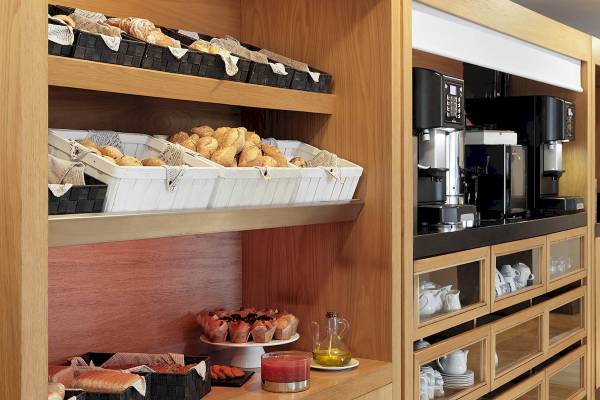 Frühstücksbereich des H10 Blue Mar Boutique Hotels mit Brot, Muffins und Kaffeemaschinen.