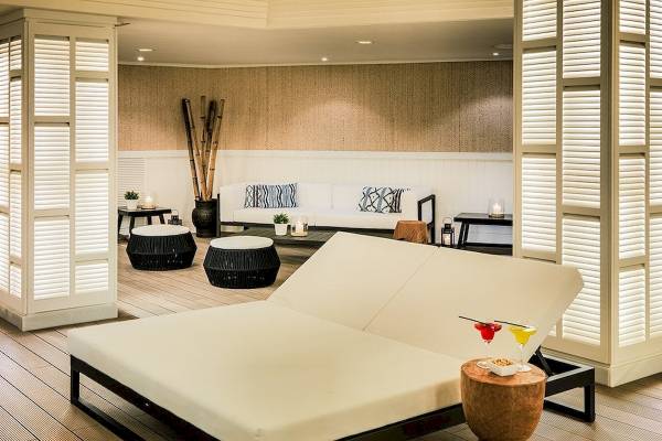 Loungebereich im H10 Blue Mar Boutique Hotel mit weißen Liegen, schwarzen Tischen und Holzboden.