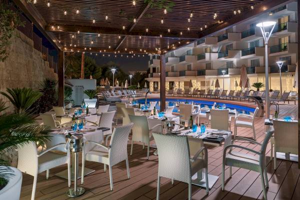 Nachtansicht der Terrasse des H10 Blue Mar Boutique Hotels mit illuminierten Tischen und Stühlen.