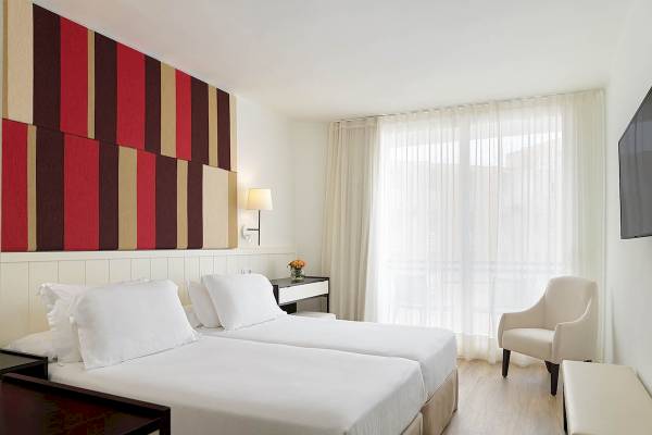 Doppelzimmer im H10 Casa del Mar Hotel mit zwei Betten, weißer Bettwäsche, einem Nachttisch, einem Stuhl und einem Fernseher.