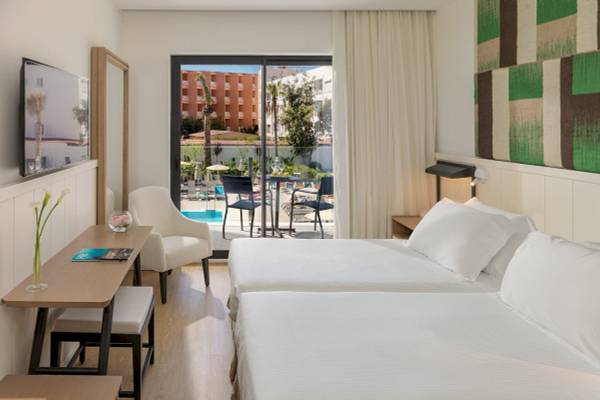 Innenansicht eines Doppelzimmers im H10 Casa del Mar Hotel mit zwei Betten, einem Tisch und Stühlen, Blick auf den Pool.