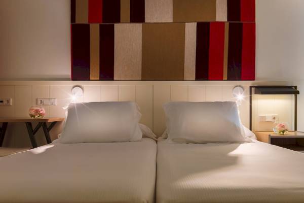 Doppelbett-Zimmer im H10 Casa del Mar Hotel mit zwei weißen Kissen und einer farbigen Wand.