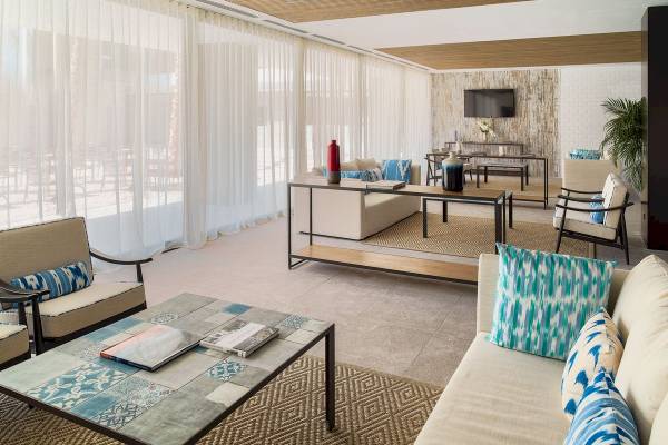 Innenansicht des Wohnbereichs im H10 Casa del Mar Hotel mit Möbeln, Tisch, Büchern und Fernseher.
