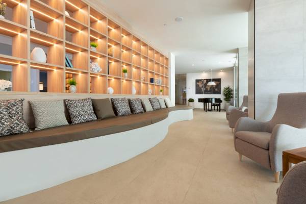 Loungebereich im Nautic Hotel & Spa mit gepolsterter Bank, Kissen, Bücherregalen und Klavier.