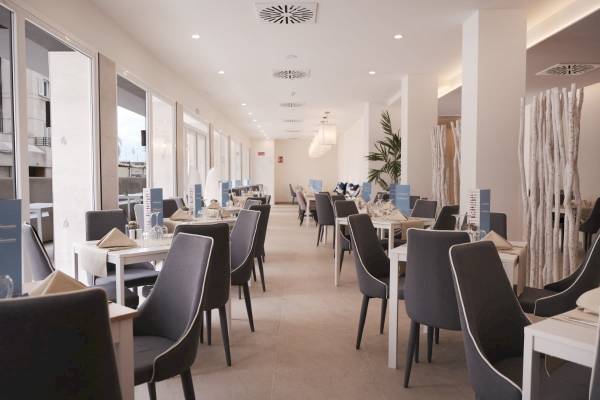 Ein elegantes Hotelrestaurant mit langen Tischen und Stühlen, hellem Dekor und großen Fenstern.