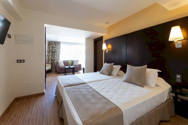 Doppelbett-Zimmer im Nautic Hotel & Spa mit zwei bequemen Betten, Kissen, Decken, Nachttischen, Lampen und Fernseher.